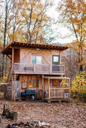 Una cabaña de madera con balcón, porche y una pequeña terraza.