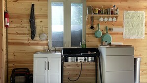 A compact kitchen with wooden walls, a sink, a stove, and a small refrigerator. - “The Summit Cabin” <br>An Off the Grid Hideaway (Barnardsville)