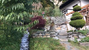 Eine Steintreppe führt zu einem Haus, am Fuße befindet sich ein kleiner Wasserfall.