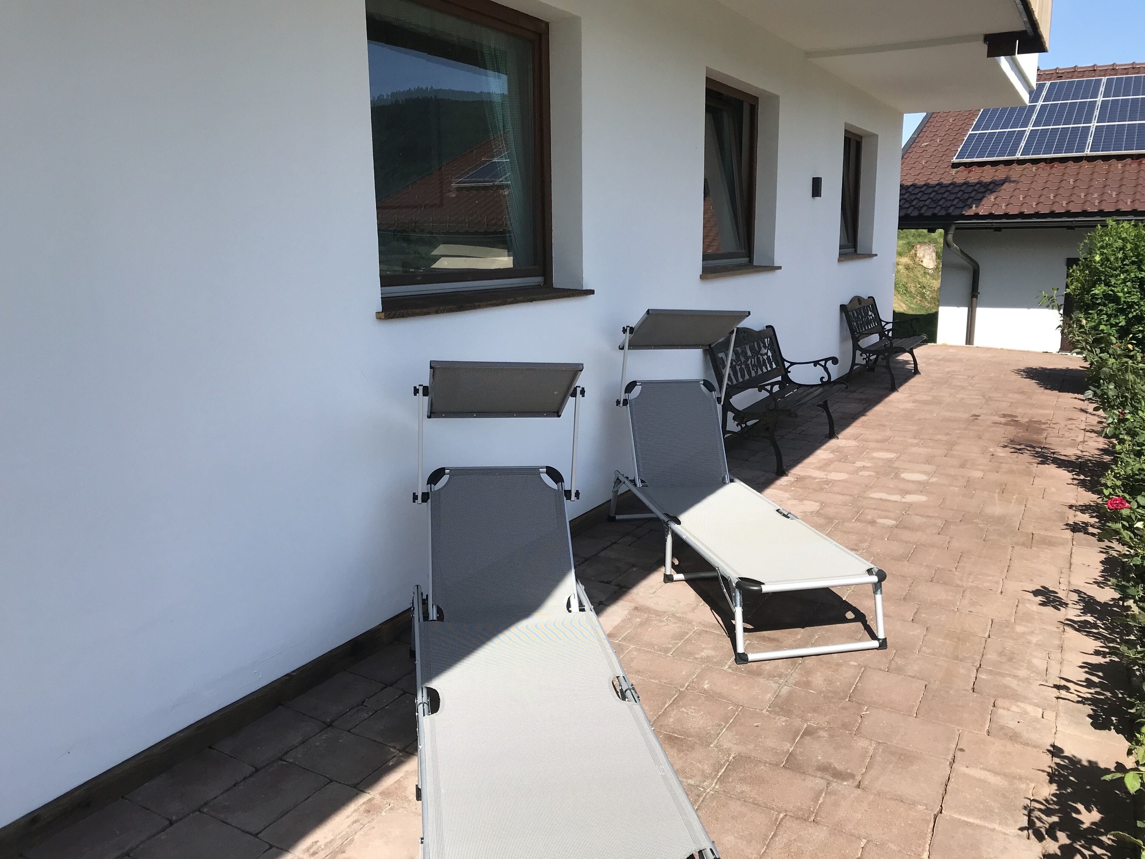 En terrasse med to liggestole, en bænk og et lille bord.
