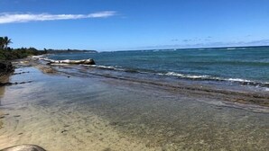Ein Strand mit klarem Wasser, einer felsigen Küstenlinie und einer entfernten Insel.