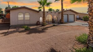 A two-story brick house with a garage, surrounded by a gravel driveway and palm trees. - Private Oasis Near Old Mesilla - Home with Pool/Spa (Las Cruces)
