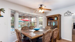 A dining area with a wooden table, patterned chairs, a ceiling fan, and a view of the outdoors. - Private Oasis Near Old Mesilla - Home with Pool/Spa (Las Cruces)