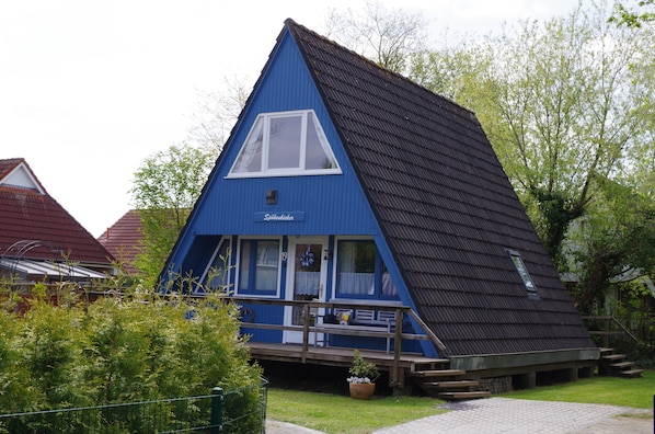 Ett blått hus med ett sluttande tak, en liten veranda och ett fönster.