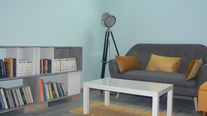 A living room with a grey sofa, a white coffee table, and bookshelves filled with books. - Maison D'hôtes Chambre Champêtre (La Chailleuse)