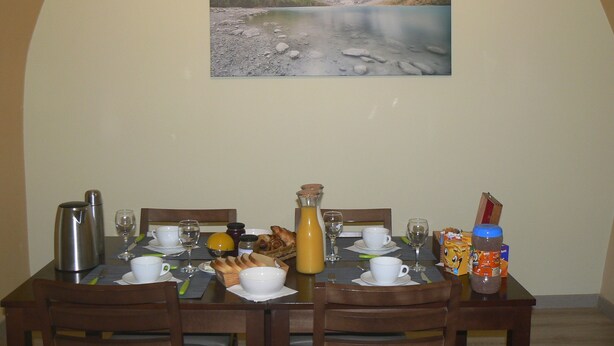 A dining table set with breakfast items, a painting of a mountainous landscape, and a view of a lake. - Maison D'hôtes Chambre Champêtre (La Chailleuse)