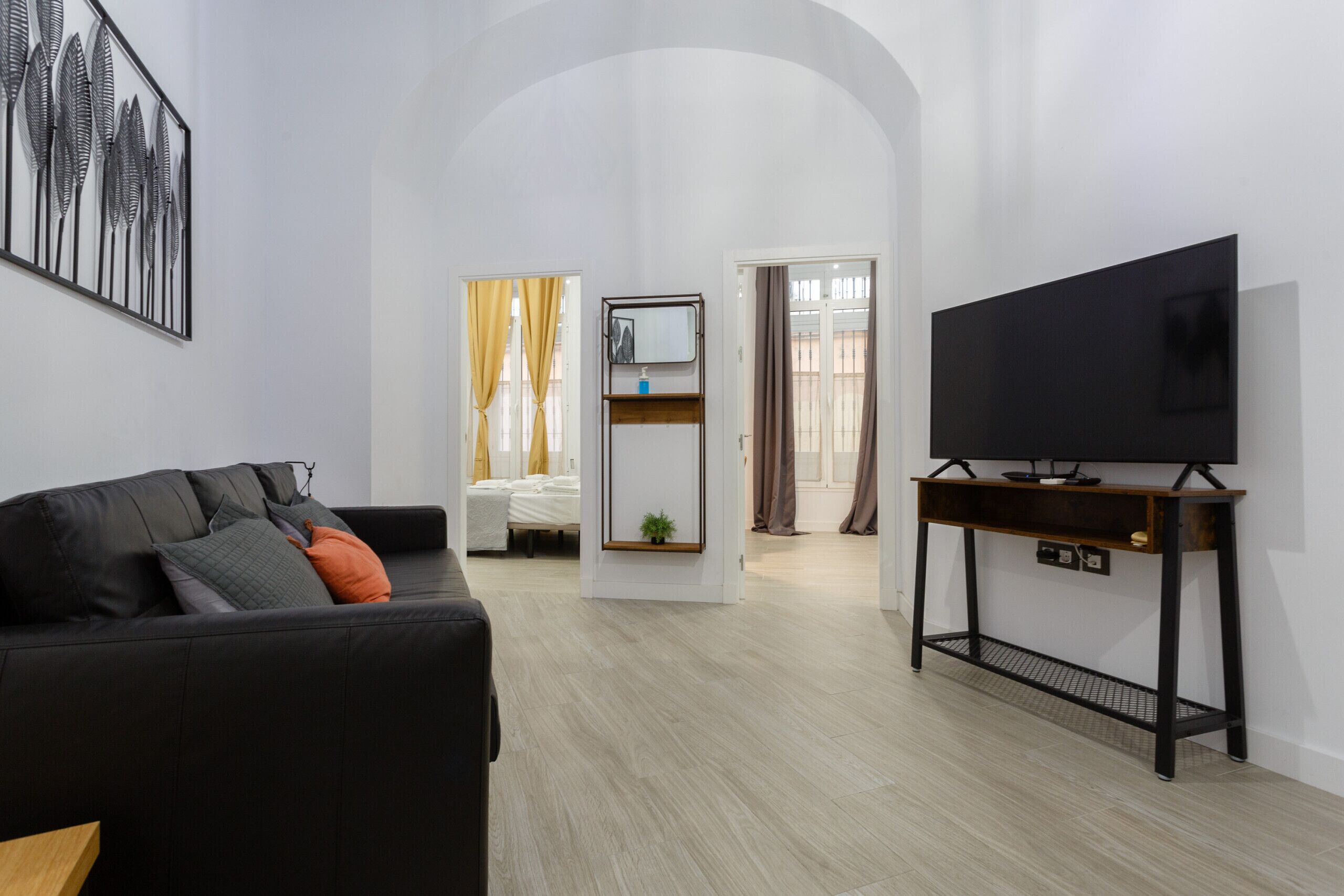 A modern living room with a black sofa, a flat-screen TV on a wooden console, and a minimalist decor.