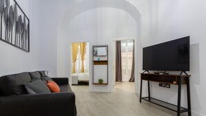 A modern living room with a black sofa, a flat-screen TV on a wooden console, and a minimalist decor. - CRUISE Adapted Apartment by Cadiz4Rentals (Cádiz)