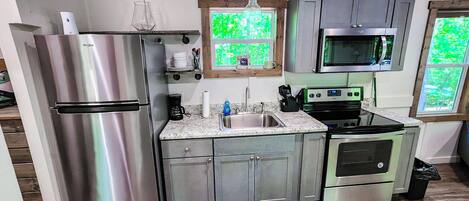 Cocina compacta con electrodomésticos de acero inoxidable, encimera de granito y piso de madera.