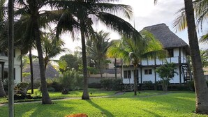 Un resort con edificios de techo de paja, palmeras y un césped bien cuidado.