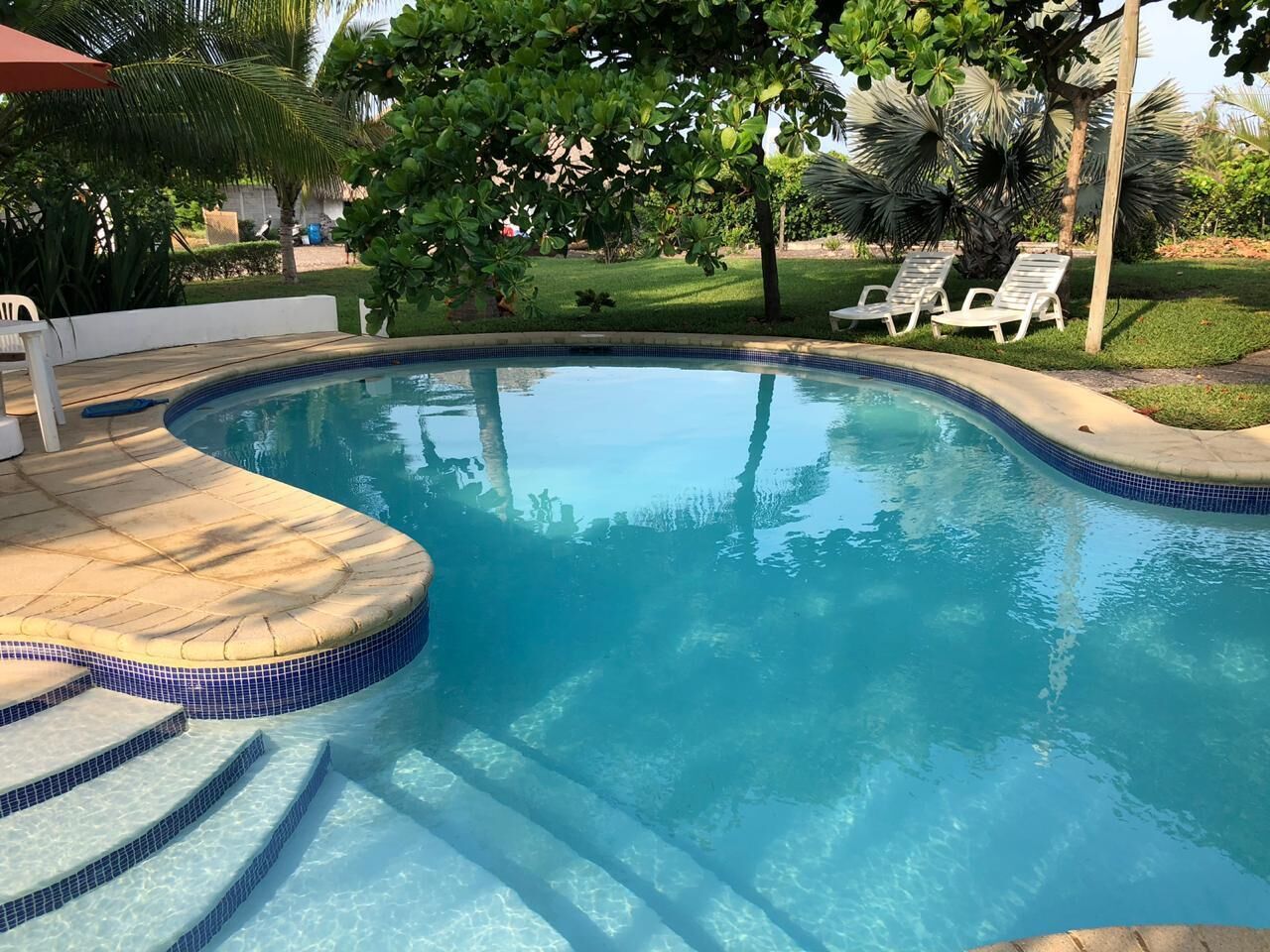 A swimming pool with clear blue water, surrounded by a tiled deck and steps leading into the pool.