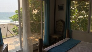Un dormitorio con cama, una silla, un escritorio de madera y vistas al océano a través de amplios ventanales.