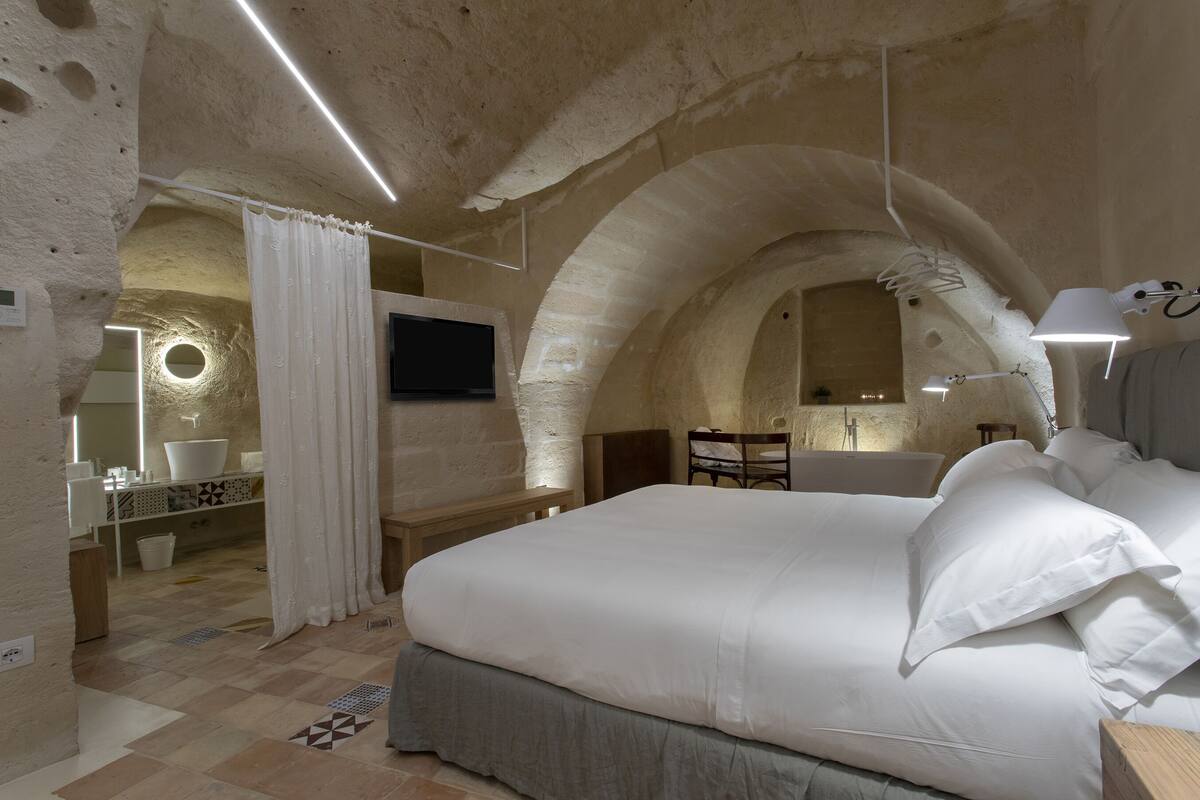 A bedroom with a large bed, a television, and a bathroom visible through an archway.