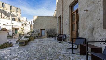 A courtyard with stone flooring, outdoor seating, and buildings with balconies.