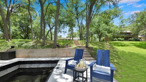 A pool area with a hot tub, lounge chairs, and a table with a beverage.