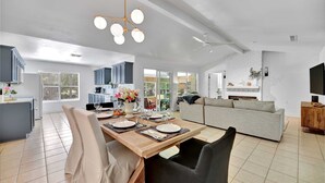 A modern living room with a sofa, a dining table set for four, and a kitchen area in the background.