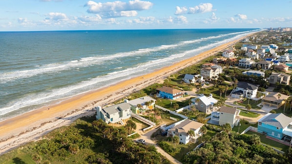 A coastal residential area with houses along the beach, a clear sky, and the ocean in the background.