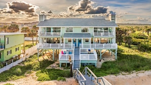 A two-story beachfront house with a balcony, a deck, and a sandy beach in the background. - Tipsy Turtle Direct Oceanfront Sunrise (Palm Coast)