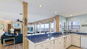 A spacious kitchen with a large island, wooden cabinets, and a view of the ocean through large windows. - Tipsy Turtle Direct Oceanfront Sunrise (Palm Coast)