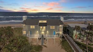A beachfront house with a balcony, a small deck, and a view of the ocean.