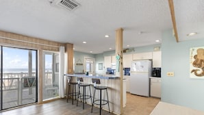 A kitchen with a bar area, a refrigerator, and a view of the ocean. - Tipsy Turtle Direct Oceanfront Sunrise (Palm Coast)