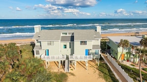A beachfront property with a two-story house featuring a balcony and a staircase leading to the beach.