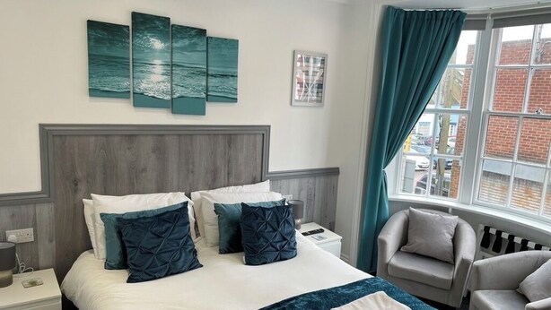 A hotel room with a bed, a nightstand, a chair, and a window with curtains. - 5 bed, 5 bath, Slps 18, Town Ho. 60 yds Weymth beach & harbour, NEWLY RENOVATED! (Weymouth)