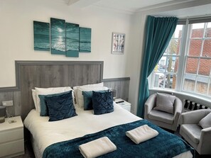 A hotel room with a bed, a nightstand, a chair, and a window with curtains.