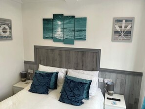 Un lit bien fait, avec deux oreillers, une table de chevet avec une lampe et un tableau au mur.