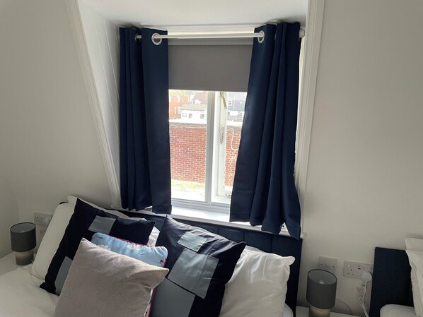 A bedroom with a bed, pillows, a window with curtains, and a view of buildings outside.