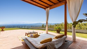 Un espace extérieur aménagé, abrité et doté d’un lit, d’une table avec un livre et une tasse, et offrant une vue sur le paysage.