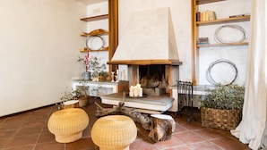Un salon chaleureux avec une cheminée, des poufs en osier et des étagères remplies de livres et d’objets décoratifs.