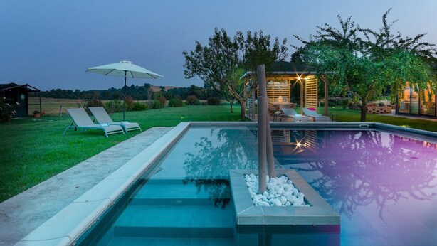 Ein Schwimmbecken mit Stufen, Liegestühlen und einer Pergola mit Beleuchtung.
