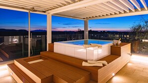 Un jacuzzi con escalones de madera y cerramiento de vidrio, con vistas a un hermoso atardecer.