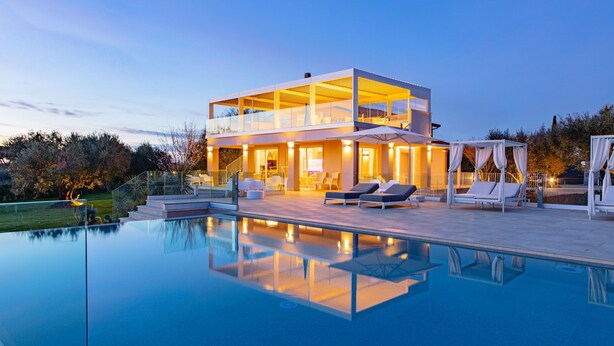 Una casa moderna de dos pisos con un balcón acristalado, piscina y mobiliario de exterior.