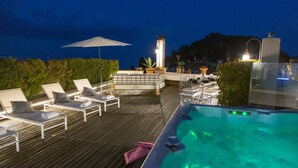 A rooftop terrace with lounge chairs, a hot tub, and a table set for dining.