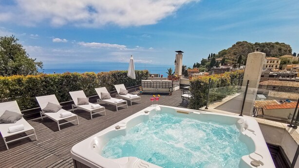 A rooftop terrace with a hot tub, lounge chairs, and a scenic view of the sea.