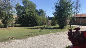 Ein Kiesweg führt zu einem Spielplatz mit Schaukel und Rutsche.