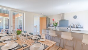 Ett modernt kök med en central köksö, en matplats med ett träbord för sex personer och ett stort fönster som släpper in naturligt ljus.