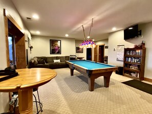 Une table de billard dans une pièce où se trouvent un canapé, une bibliothèque et un téléviseur.