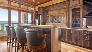 A kitchen with a bar area, wooden cabinets, and large windows overlooking a body of water.