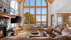 A spacious living room with a stone fireplace, leather sofa, and large windows overlooking a body of water.