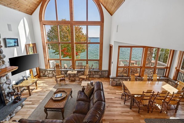 A spacious living area with a large wooden table and comfortable seating, overlooking a body of water through large windows.