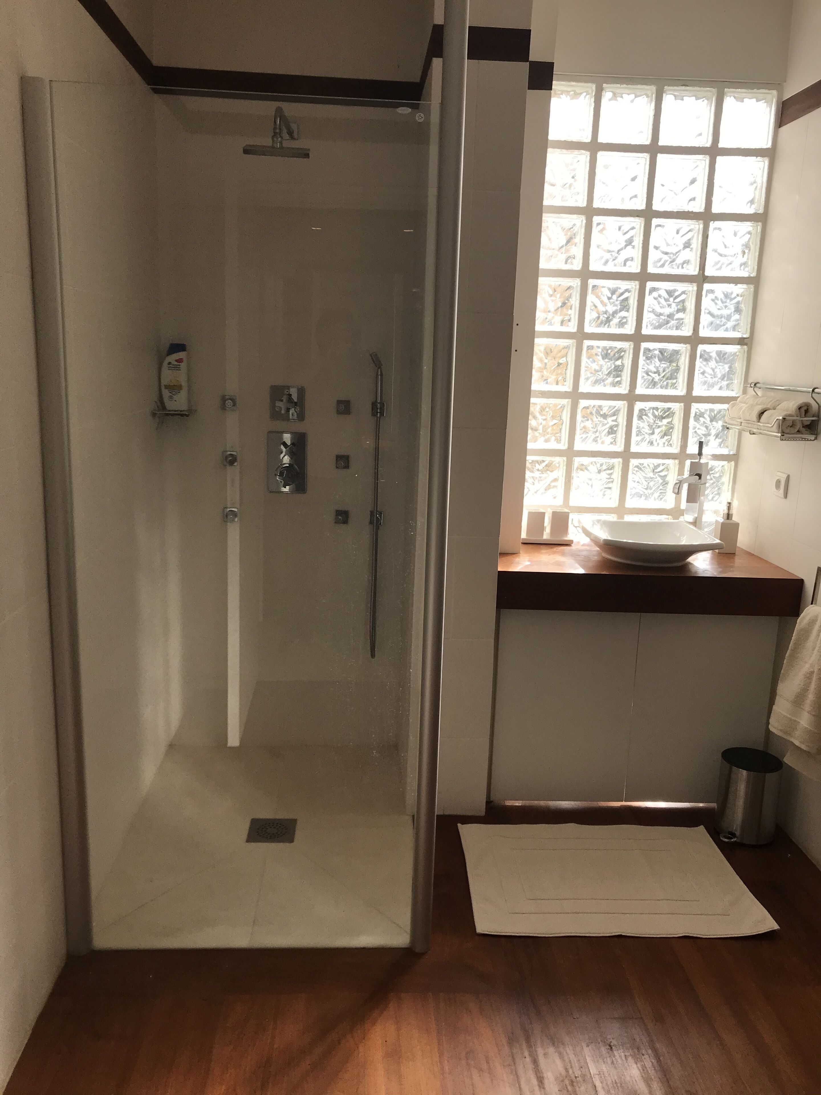 A modern bathroom with a glass-enclosed shower, a wooden vanity with a sink, and a window with frosted glass panels.