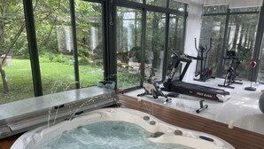 Un área de spa con un jacuzzi, equipo de ejercicio y vistas a un jardín a través de amplios ventanales.