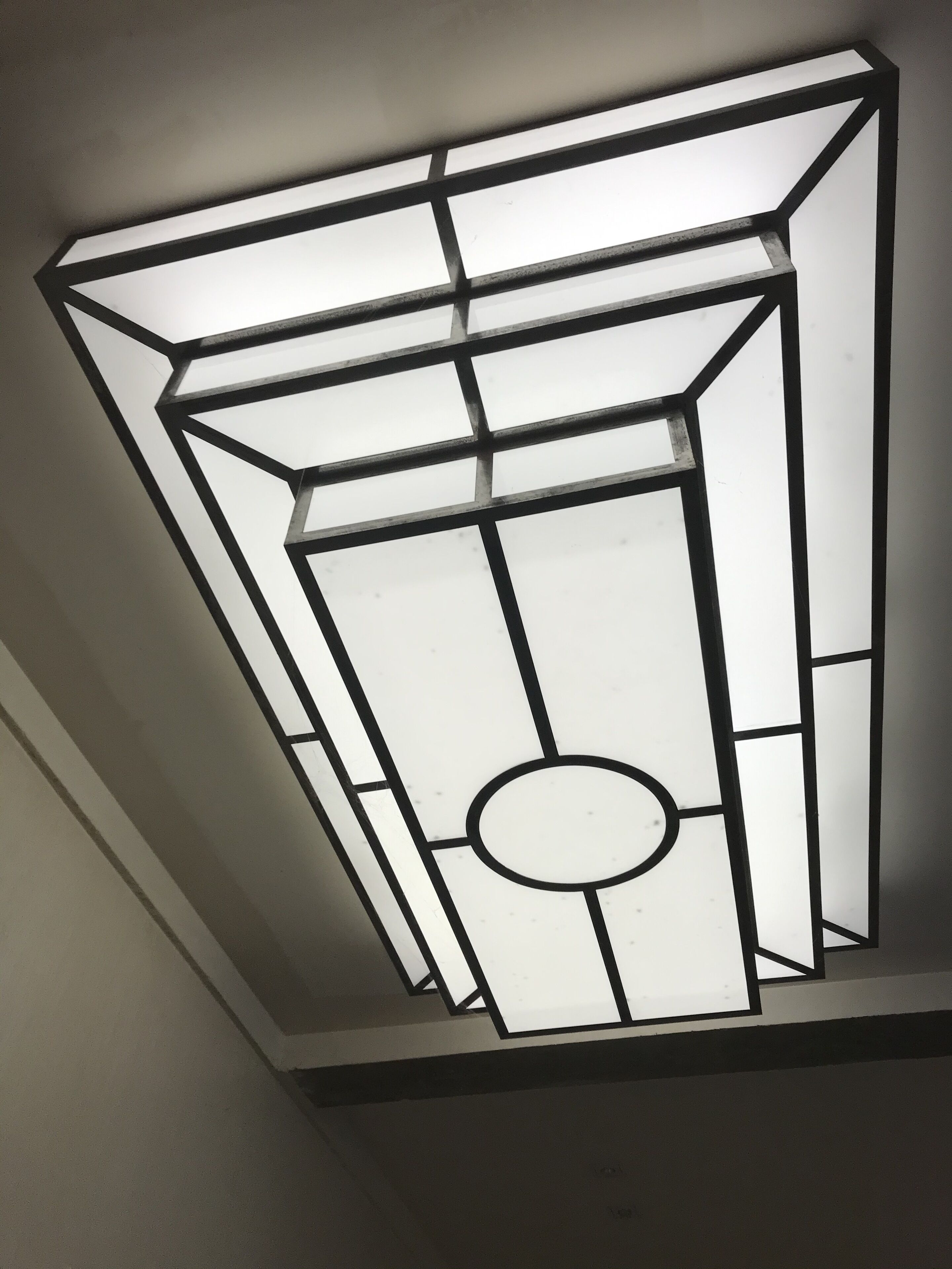 A ceiling light fixture with a geometric design and a central circular element.