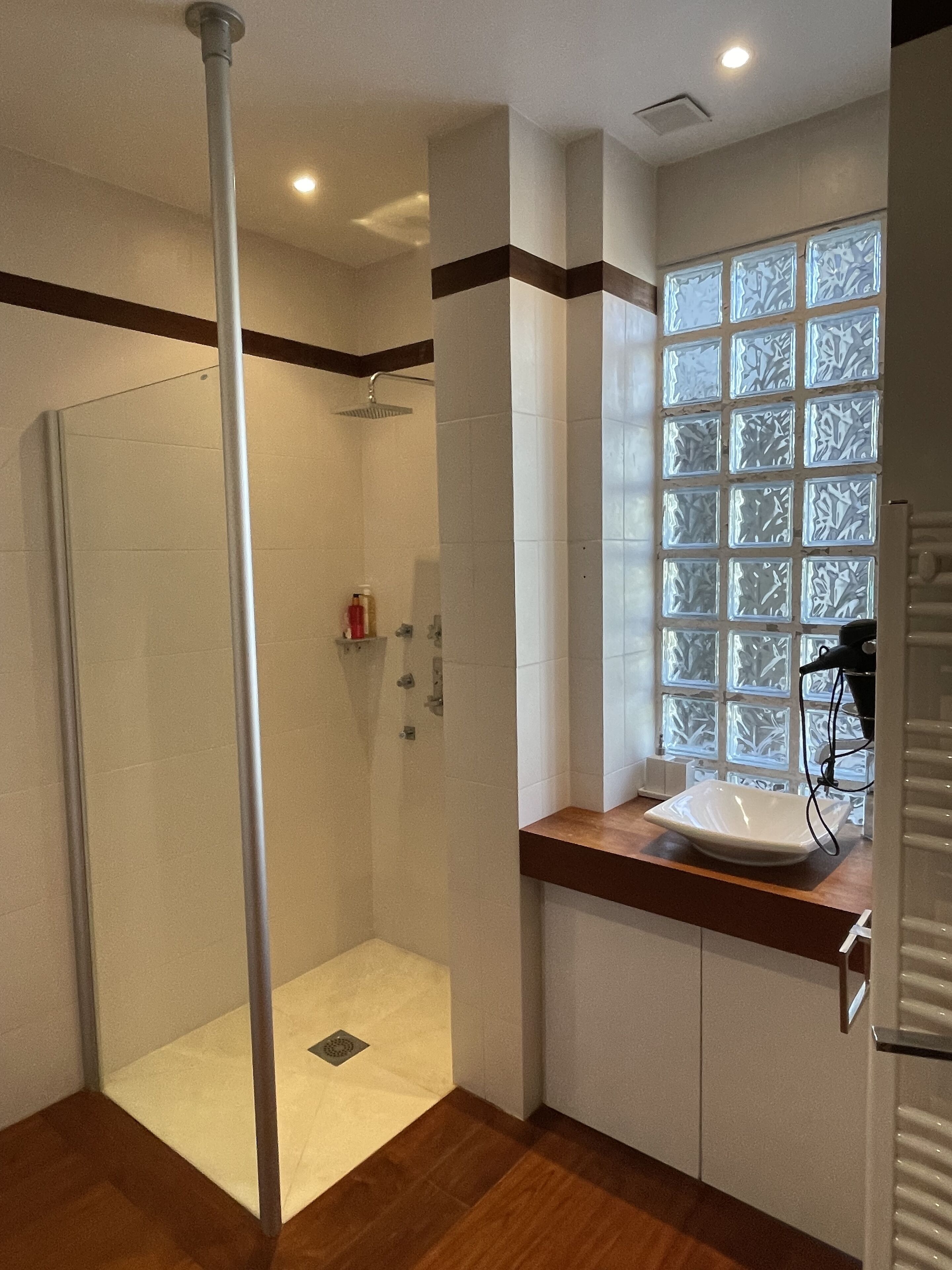 A modern bathroom with a glass shower enclosure, a sink with a wooden countertop, and a decorative window with frosted glass panels.