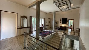 Un interior espacioso con techos altos, una escalera con barandillas de cristal y vistas al exterior a través de amplios ventanales.