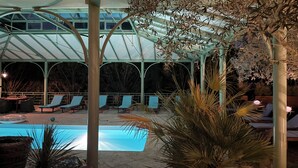 Un espacio al aire libre techado con piscina, sillas de descanso y plantas en macetas.