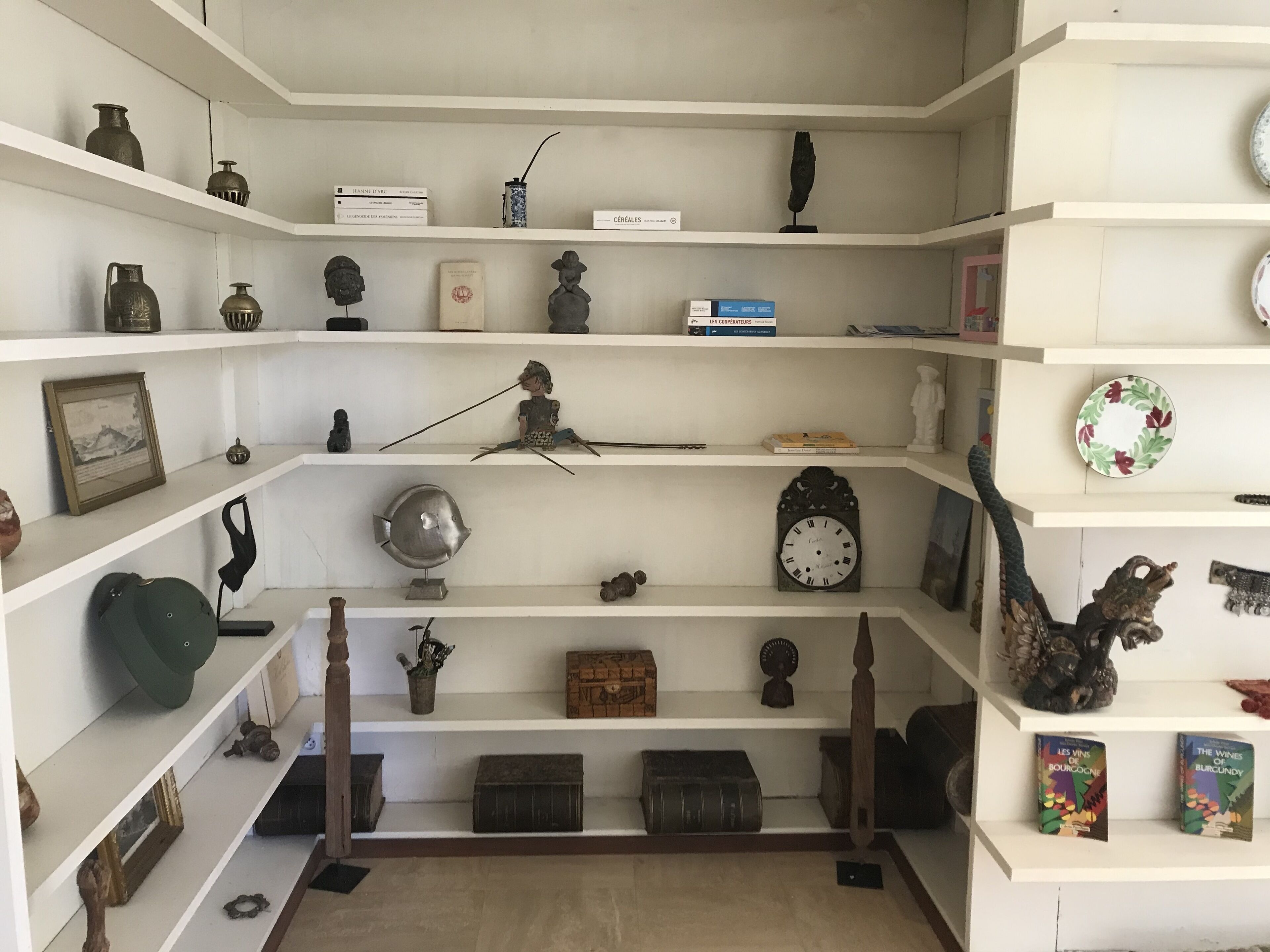Una stanza con diverse mensole bianche piene di libri, figurine e oggetti decorativi.